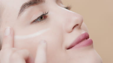 Gorgeous young European woman applies moisturizer under her eyes