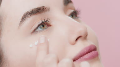 Beautiful young Caucasian woman applies day cream under her eye