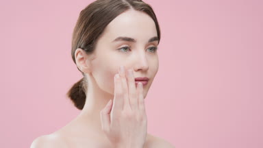 Slim young woman puts face care cream on her cheek smiling wide