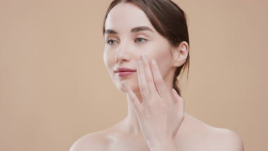 Fit Caucasian girl applies face cream on her cheek smiling wide