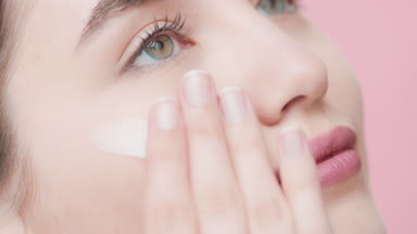 Good-looking woman applies moisturizer under eye smiling wide