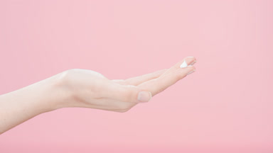 Skin care model lifts hand with a drop of cream on forefinger up