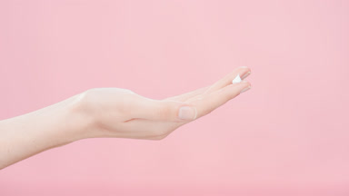 Skin care model lifts hand with a drop of cream on forefinger up