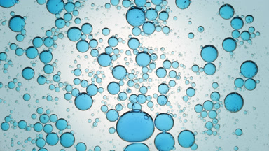 Blue different sized bubbles move in spiral in clear liquid