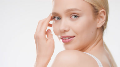 European young golden-haired woman touches face smiling wide