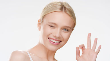 Cute young blonde woman shows OK sign winking and smiling wide