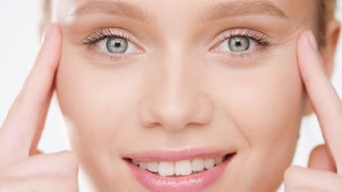 Female model with golden hair lifts eyes with fingers smiling