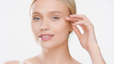 Woman in white top turns to the camera touching face and smiling