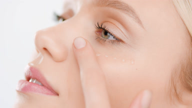 Pretty woman with golden hair applies skin care serum on cheek