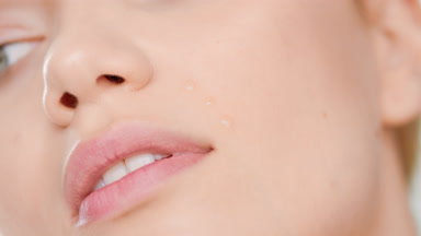 Caucasian female skincare model puts face care serum on cheek