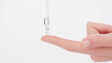 Drop of skincare serum falls down from dropper on forefinger