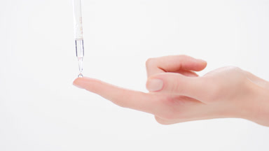 Drop of transparent liquid falls down from dropper on forefinger