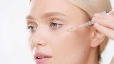 European woman applies face care serum on cheek from dropper