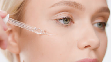 Caucasian blond woman puts skin care serum on cheek from dropper