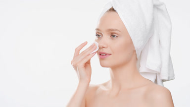 Gorgeous woman touches cheek with cotton pad and smiles wide