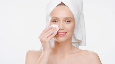 Pretty young woman touches cheek with cotton pad smiling wide