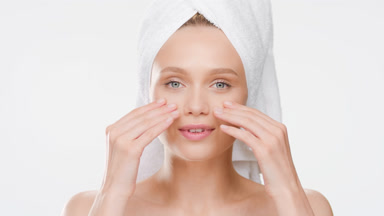 Cute woman with towel on head touches cheeks and smiles wide