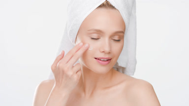 Woman applies moisturizer on face turning to camera and smiling