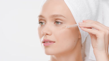 Beautiful female model applies face serum on cheek from dropper