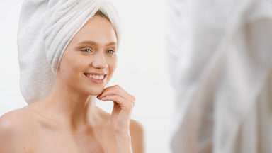 Cute slim girl touches face smiling wide in front of the mirror