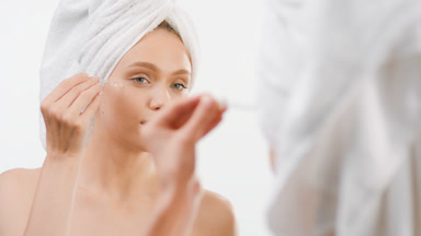 Woman applies serum on face using a dropper in front of mirror