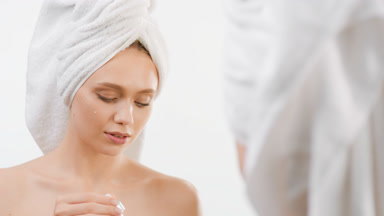 Woman puts face serum on cheek and smiles in front of the mirror