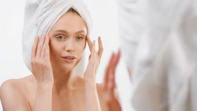 Attractive fit young woman taps eye cream in front of the mirror