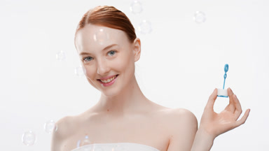 European woman with long red hair blows soap bubbles smiling