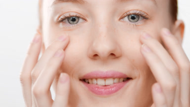 Young Caucasian female skin care model massages cheeks smiling