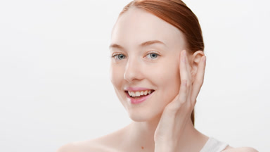 Gorgeous woman with ginger hair in ponytail touches face smiling