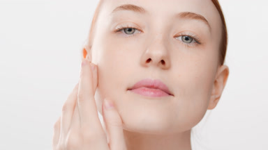 Caucasian young red-haired female skin care model touches face