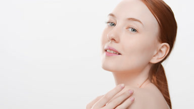 Woman with long red hair touches jawline and shoulder smiling