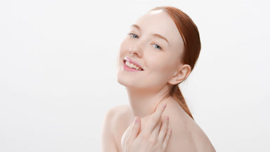 Slim young woman with long ginger hair touches shoulder smiling
