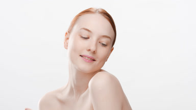 Young woman with bare shoulders touches face averting eyes down