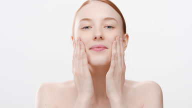 Red-hair woman with bare shoulders touches cheeks smiling wide