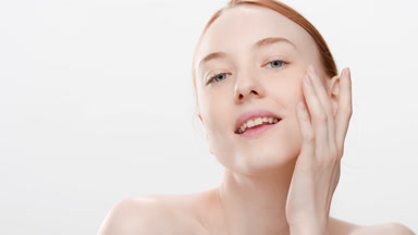 Red-haired woman with bare shoulders touches jawline smiling