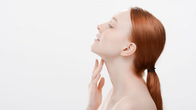 Redhead woman touches her chin and neck standing sideways and looking up on white background