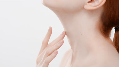 Slim female model touches chin, neck and chest standing sideways