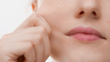 Female face care model stretching her skin on white background