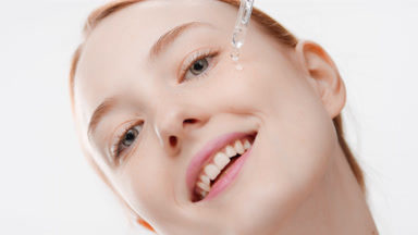 Pretty fit woman drips serum from dropper on cheek smiling wide