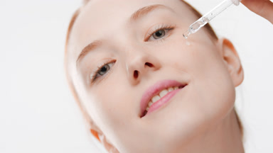 Cute woman drips skin care serum from dropper on cheek smiling