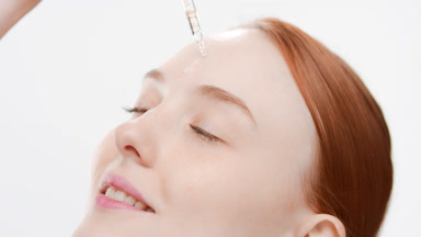 Fit woman drips serum on forehead smiling wide and closing eyes