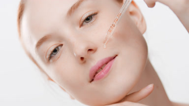 Young woman drips skin care serum from dropper on cheek smiling