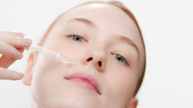 Woman drips serum from dropper on cheek smiling and closing eyes