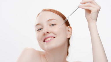 Young woman drips face care serum from dropper on cheek smiling