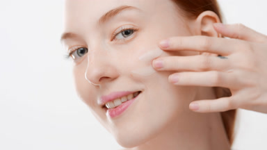 Fit woman with rusty hair puts anti-aging cream on cheek smiling