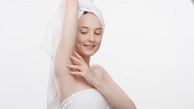 Woman wrapped in a towel touches body and looks at the camera