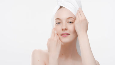Young slim woman with a towel on head touches face smiling wide