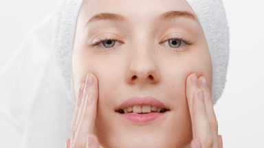 Fit woman with a towel on hair stretches facial skin smiling