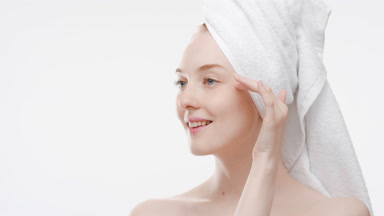 Woman with a hair towel touches nose, cheek and jaw line smiling